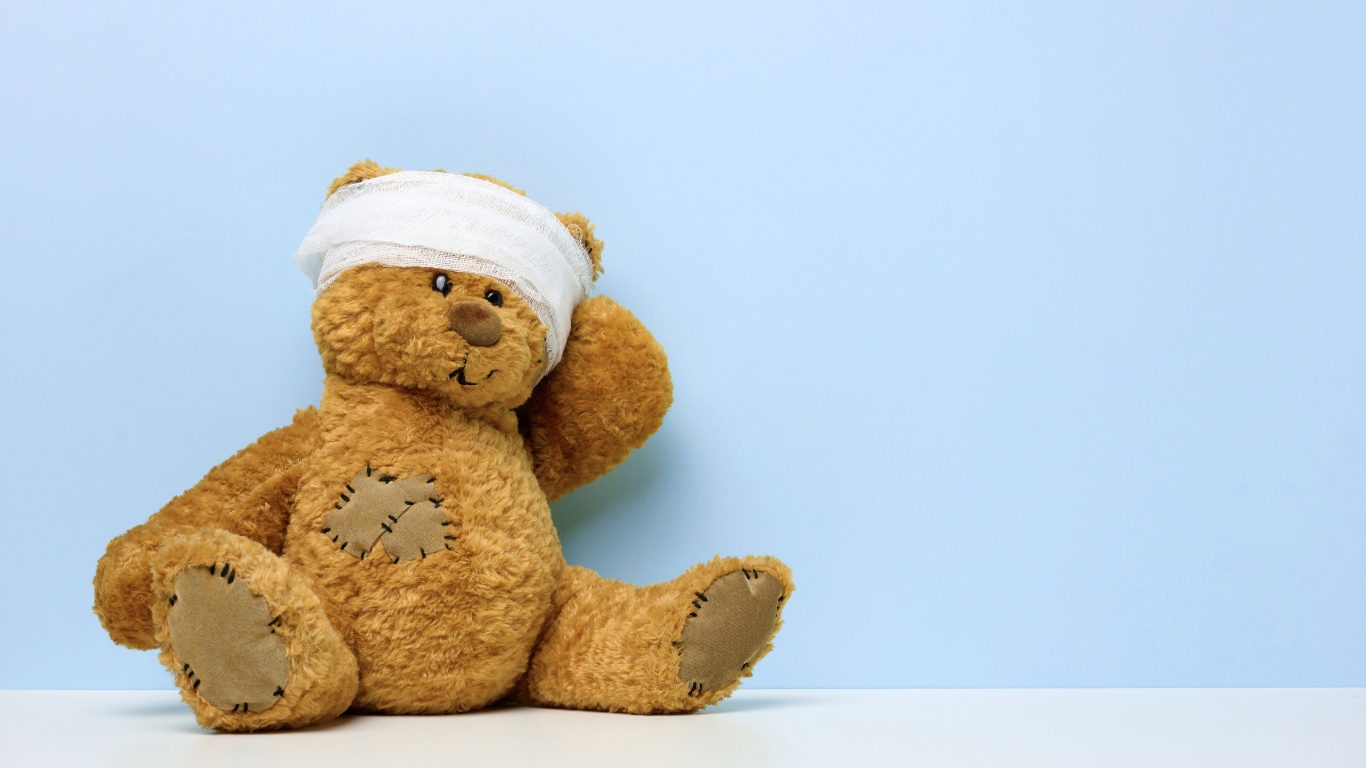 Teddybär mit Kopfverband vor hellblauem Hintergrund – Symbolbild für seelische Verletzungen aus der Kindheit